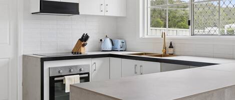 A modern kitchen with white cabinetry, a black countertop, a built-in oven, and a window with a view of greenery.