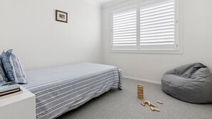 Une chambre avec un lit, un fauteuil poire et une fenêtre avec des stores.