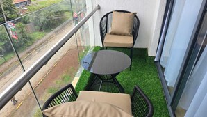 A balcony with a glass railing, two wicker chairs with cushions, a small round table, and artificial green grass. - Ideal Homes by Lyn is an executive 1 bedroom bnb located at the heart of Nairobi (Nairobi)