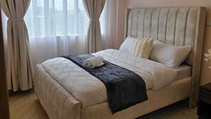 A bedroom with a bed, curtains, a headboard, and a patterned rug. - Ideal Homes by Lyn is an executive 1 bedroom bnb located at the heart of Nairobi (Nairobi)