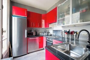 Una cuina amb armaris vermells, electrodomèstics d'acer inoxidable i un taulell negre.