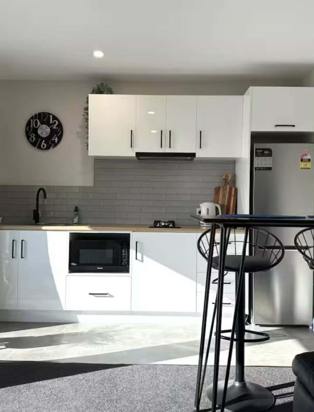 A modern kitchen with white cabinets, a microwave, a refrigerator, and a clock on the wall.