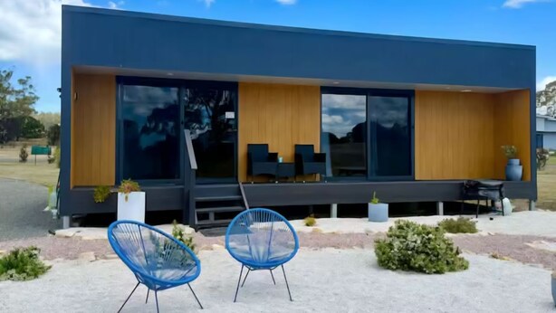 A modern building with large windows, a flat roof, and a patio area with chairs.