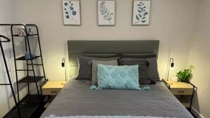 A bedroom with a bunk bed, a bed with pillows, a bedside table, a lamp, and wall art.