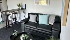 A living area with a black sofa, a small round coffee table, and a dining table with two chairs.
