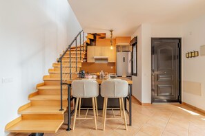 Une cuisine moderne avec un escalier en bois, un coin repas avec deux chaises et un réfrigérateur.
