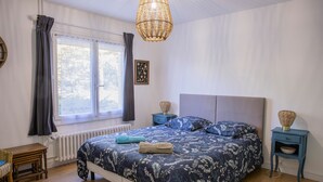 Un dormitorio con una cama, una ventana con cortinas, una mesita de noche con lámpara y un radiador.
