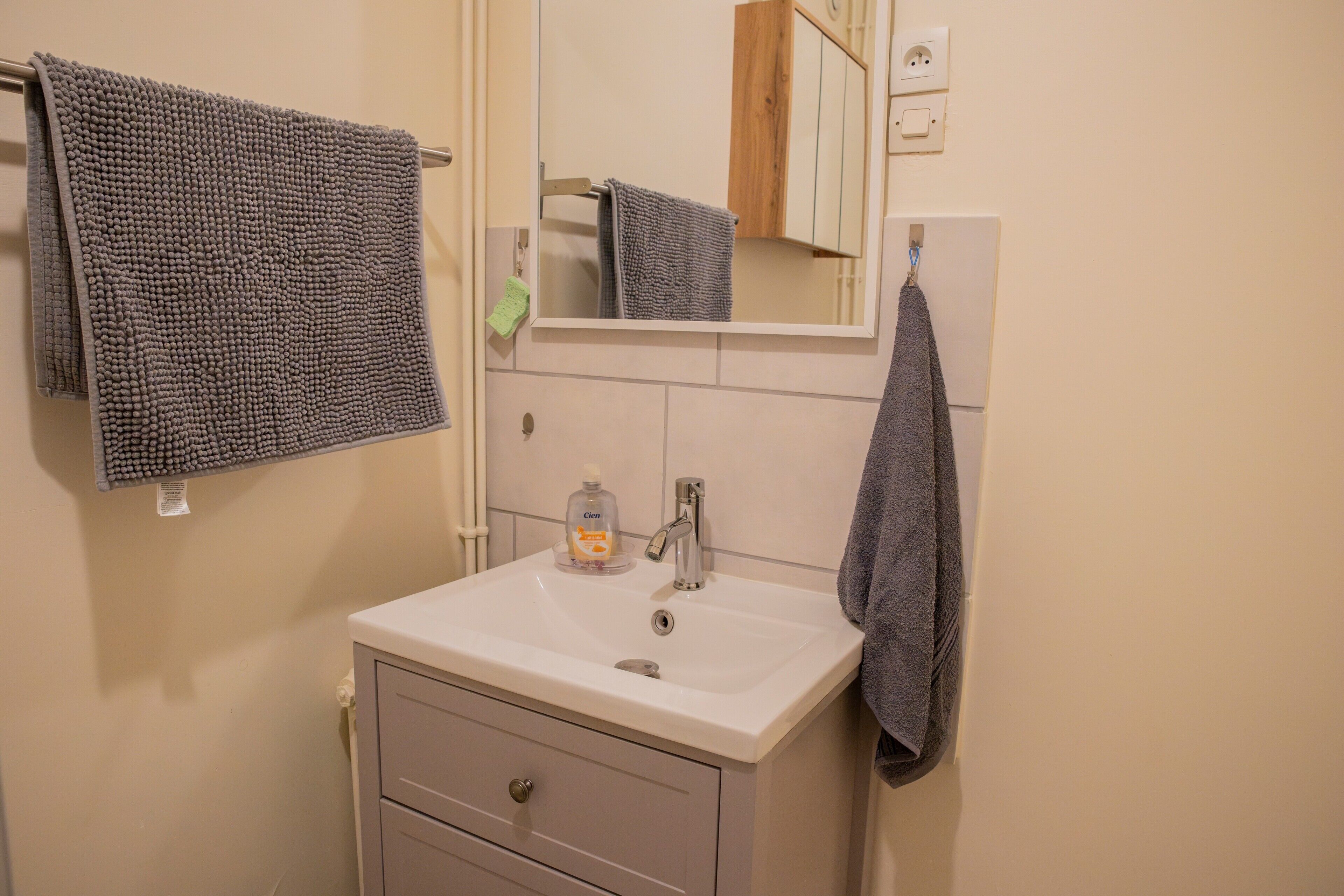 A bathroom with a white sink, a mirror, and two towels hanging on the wall.