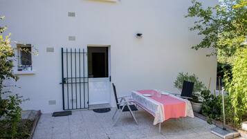 A white building with a door, a window, a table with a checkered tablecloth, and potted plants.