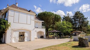 Una casa de dos pisos con un porche cubierto, un jardín y un árbol grande.