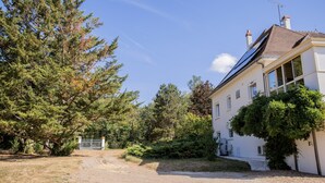 Una casa con camino de grava, una reja y un árbol grande al frente.