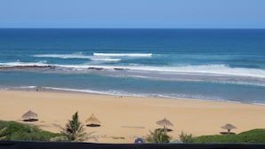 Ein Strand mit Wellen, Sonnenschirmen und blauem Himmel.