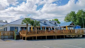 A beachfront property with a wooden deck, palm trees, and a blue-roofed building. - "Catch of the Day" 2bdr 1.5bth -Water Front Home @Pier 98 Marina...BOOK TODAY (Panama City)