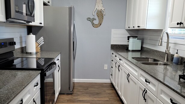 A kitchen with white cabinets, a stainless steel refrigerator, a microwave, and a wooden floor. - "Catch of the Day" 2bdr 1.5bth -Water Front Home @Pier 98 Marina...BOOK TODAY (Panama City)