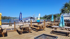 A wooden deck with picnic tables and a fire pit, overlooking a marina with boats and a building labeled 'Pier 98 Marina Bait & Tackle.' - "Catch of the Day" 2bdr 1.5bth -Water Front Home @Pier 98 Marina...BOOK TODAY (Panama City)