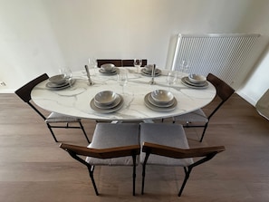 Una mesa redonda de comedor con seis sillas, cada una con asiento acolchado y respaldo de madera. La mesa está dispuesta con platos, tazones y copas de vino.