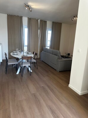 Een moderne woonkamer met een eethoek, een grijze bank en houten vloeren.
