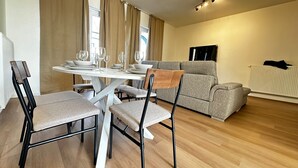 Ein modernes Wohnzimmer mit Esstisch für vier Personen, einem grauen Sofa und einer Heizung.