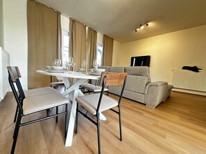 A modern living room with a dining table set for four, a grey sofa, and a radiator. - Chic 2 Apartments Near to City Center (Ghent)