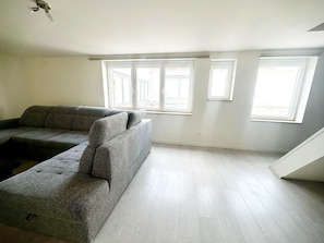 Una habitación con un sofá seccional gris, ventanas amplias y piso de madera.
