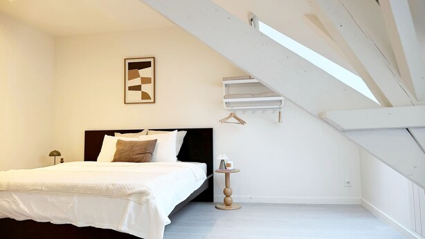 Ein Schlafzimmer mit einem Bett, einem Nachttisch, einer Hängelampe, einem an der Wand montierten Regal und einer Decke mit freiliegenden Balken.