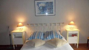 A bed with striped pillows, two bedside tables with lamps, and a framed picture on the wall. - Gîte Familial au Coeur du Triangle Vert - Piscine et Détente Assurées (Borey)
