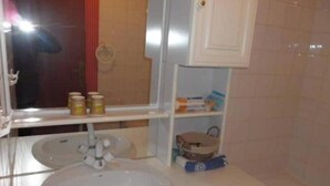 A bathroom with a white sink, a mirror, a shelf with jars, and a cabinet. - Gîte Familial au Coeur du Triangle Vert - Piscine et Détente Assurées (Borey)