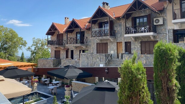 A multi-story building with stone facade, balconies, and outdoor seating areas. - Cozy mountain apartment in Platres (Pano Platres)