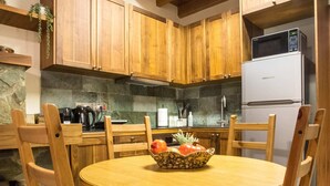 A wooden kitchen with a round table, chairs, a microwave, and a refrigerator. - Cozy mountain apartment in Platres (Pano Platres)