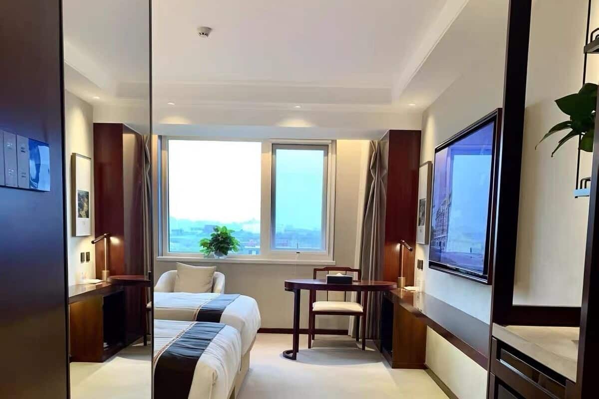 A hotel room with a large bed, a desk, a chair, a TV, and a window with a view.