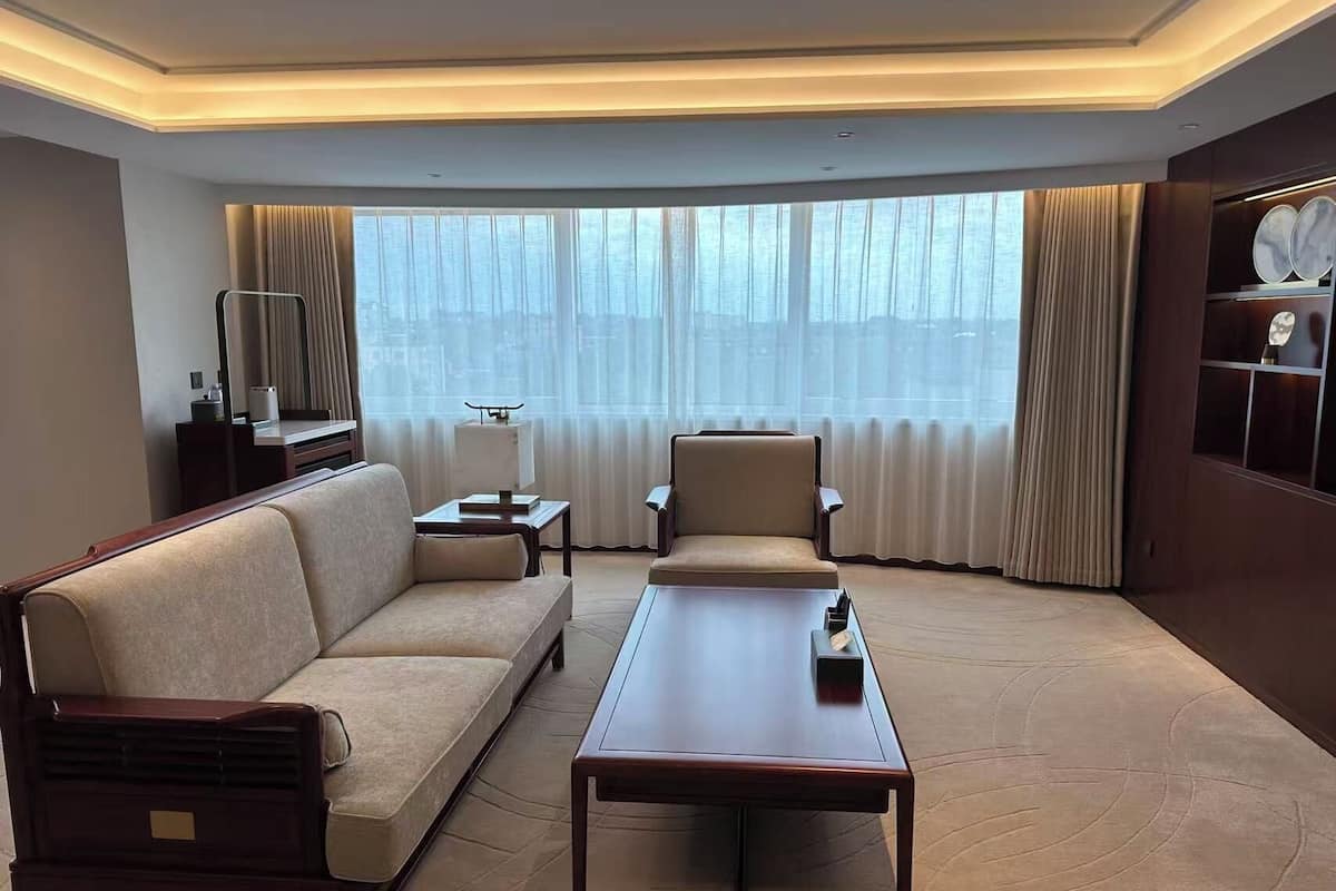 A hotel room with a sofa, armchair, coffee table, and a large window with curtains.