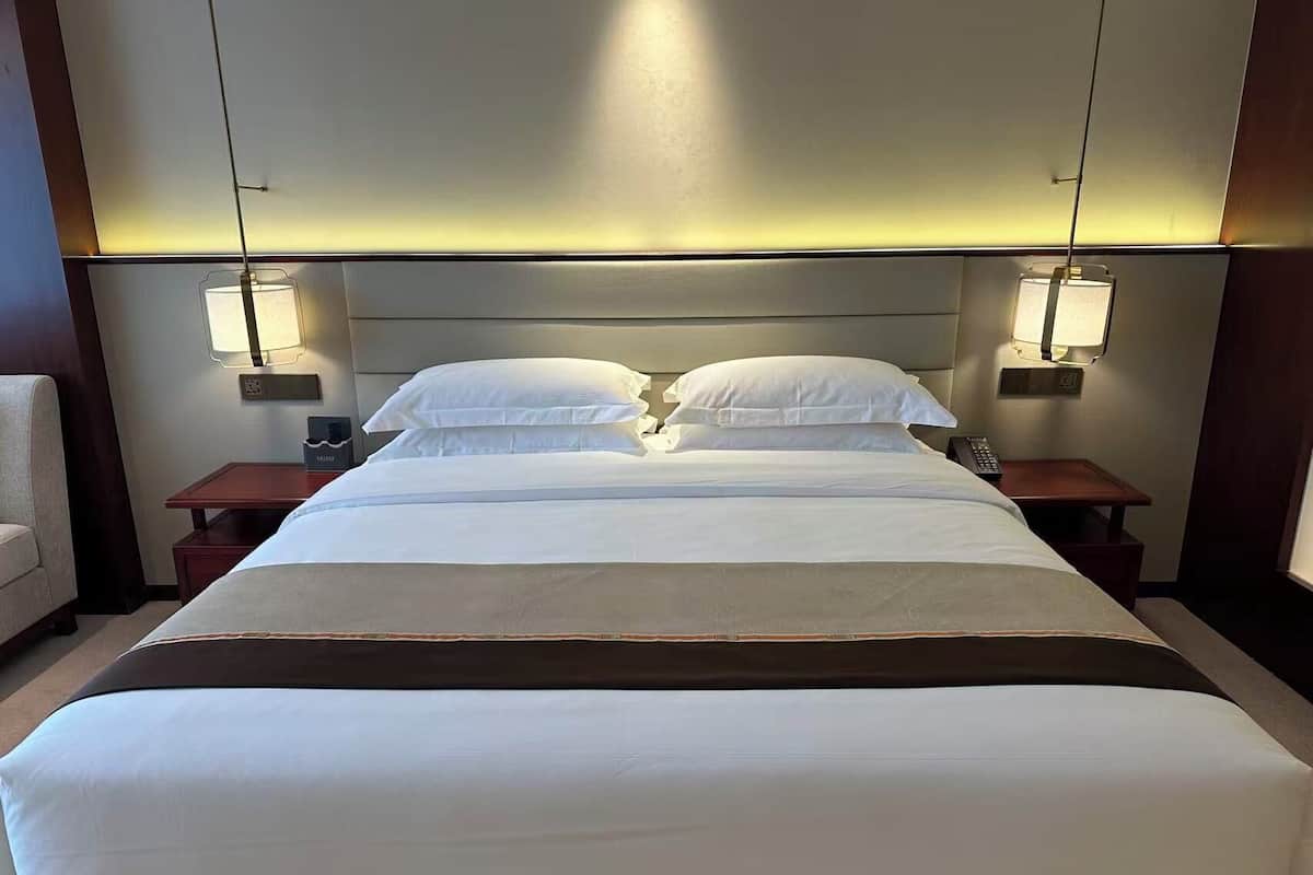 A hotel room with a large bed, two bedside tables, a chair, and wall-mounted lamps.