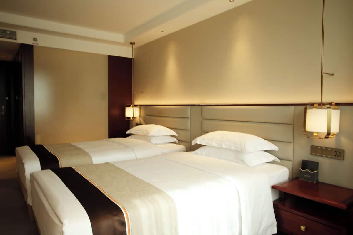 A hotel room with two beds, a nightstand, and a wall-mounted lamp.
