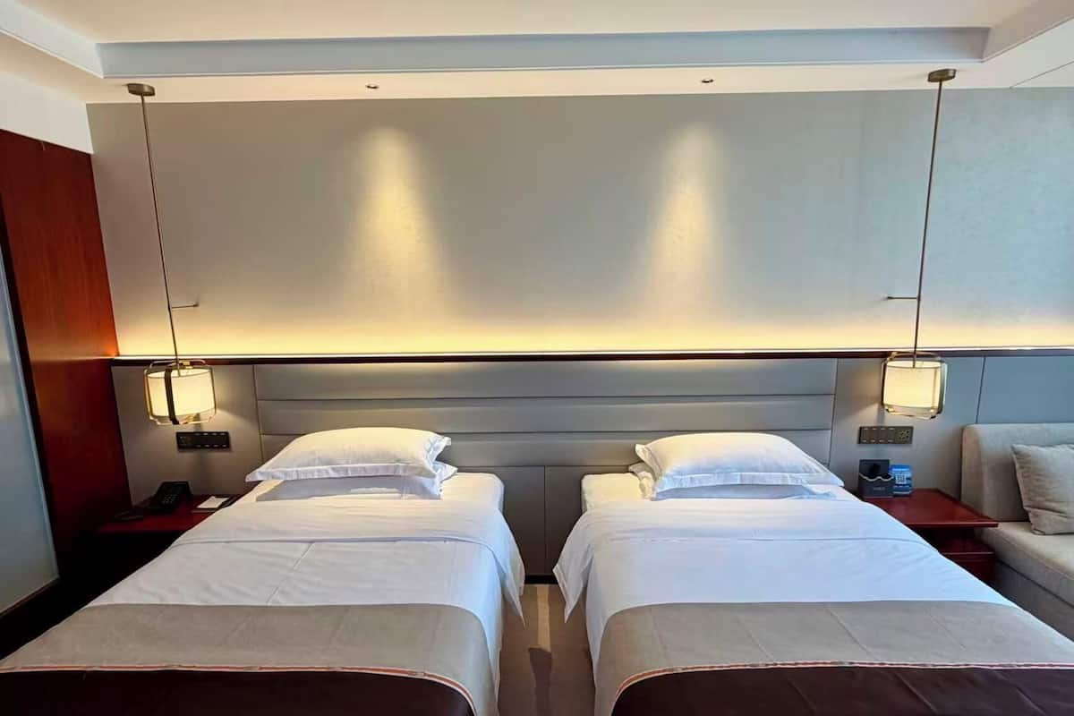 A hotel room with two beds, a bedside table with a phone, and a wall-mounted light fixture.