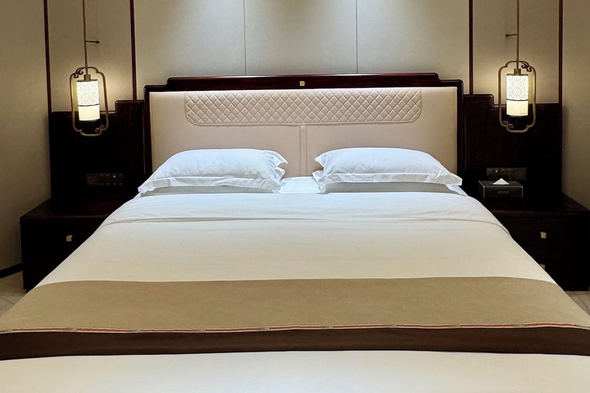 A hotel room with a large bed, two bedside tables, and a ceiling light fixture.