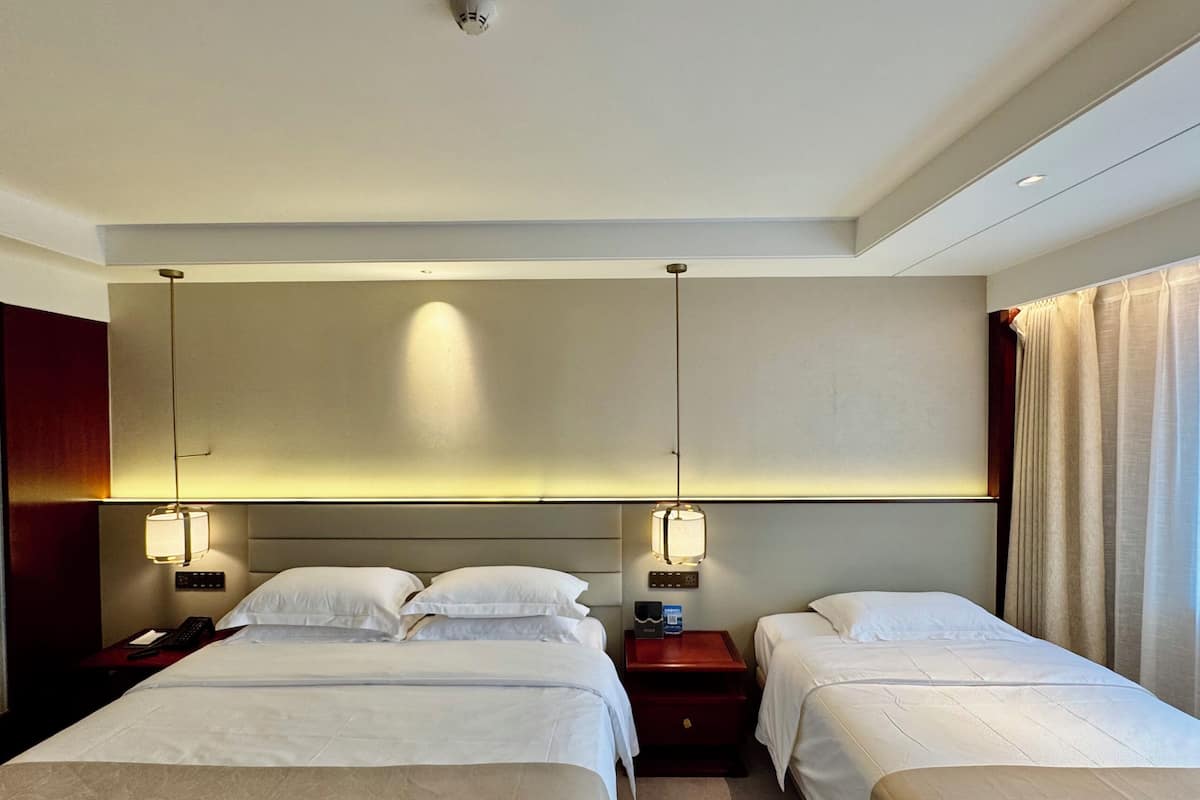 A hotel room with two beds, a headboard, bedside tables, lamps, and a ceiling light fixture.