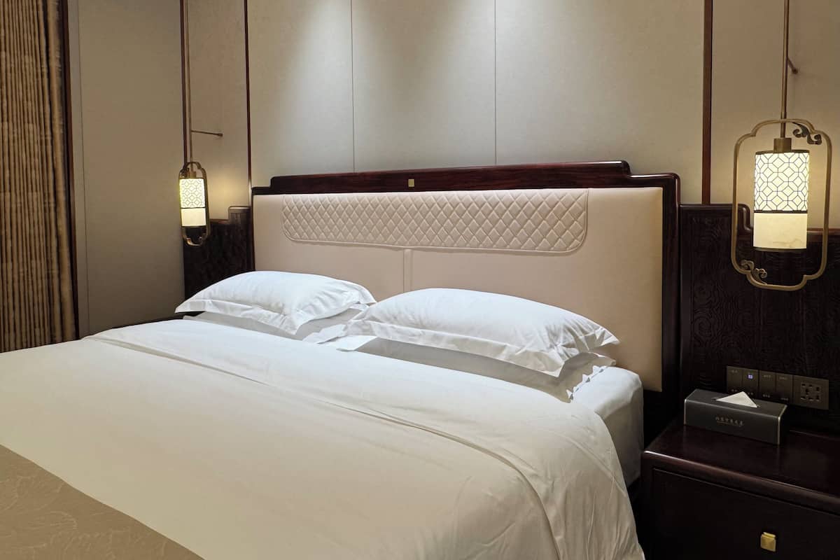 A hotel room with a large bed, a headboard with a quilted design, bedside lamps, and a nightstand with a tissue box.