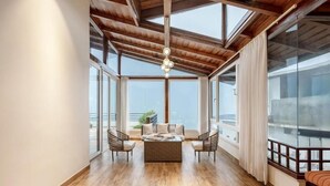 A spacious balcony with a wooden ceiling, large windows, and a seating area with a table. - ELIVAAS Antarmann Casa Zenith 6 BHK (Bhimtal)