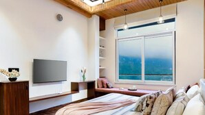 A bedroom with a bed, a TV, a window with a view, and a wooden ceiling. - ELIVAAS Antarmann Casa Zenith 6 BHK (Bhimtal)