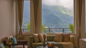 A living room with a sofa, a coffee table, and a view of mountains through large windows. - ELIVAAS Antarmann Casa Zenith 6 BHK (Bhimtal)