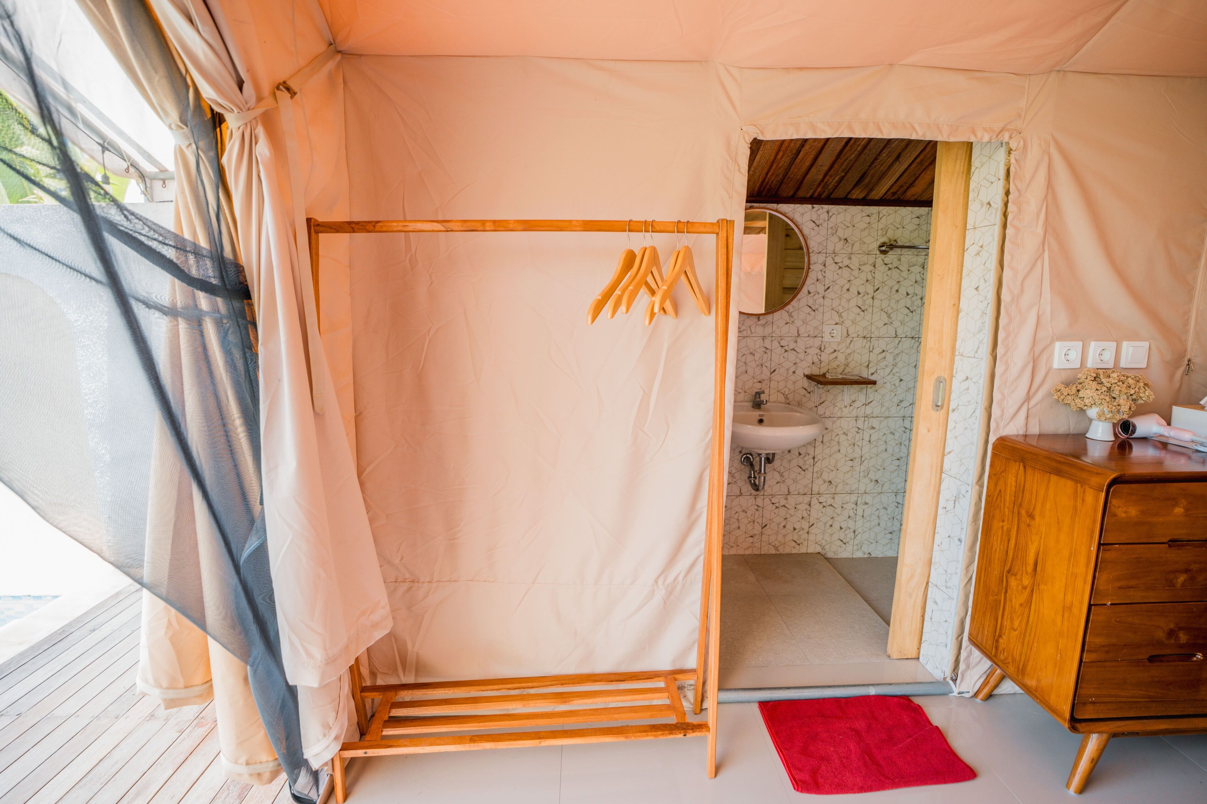 A tented room with a shower, wooden furniture, and a bathroom with a sink and mirror.