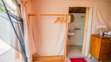 A tented room with a shower, wooden furniture, and a bathroom with a sink and mirror.