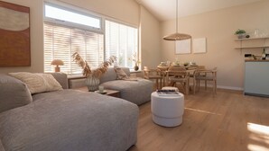 Un salon moderne comprenant un canapé, un pouf, une table à manger, des chaises et un coin cuisine avec un comptoir et des étagères.