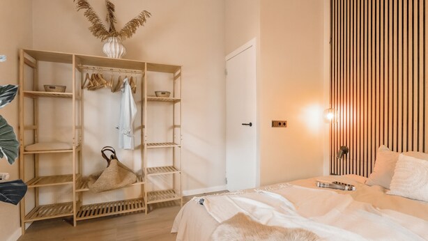 Une chambre à coucher comprenant un lit, une armoire, un portant et une table de chevet.