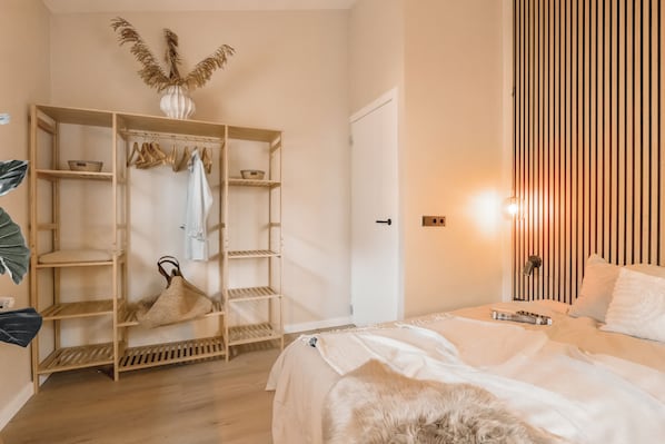 Une chambre à coucher comprenant un lit, une armoire, un portant et une table de chevet.