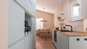 Une cuisine moderne avec un coin repas, comprenant une table en bois, des chaises, des luminaires suspendus et des appareils électroménagers intégrés.