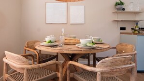 Une table de salle à manger ronde en bois, accompagnée de six chaises en osier, un luminaire suspendu en fibres tressées et deux œuvres d’art abstraites fixées au mur.