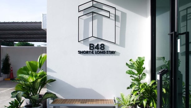 A modern building exterior with a logo, a bench, and potted plants. - B48 Hotel (Bangkok)