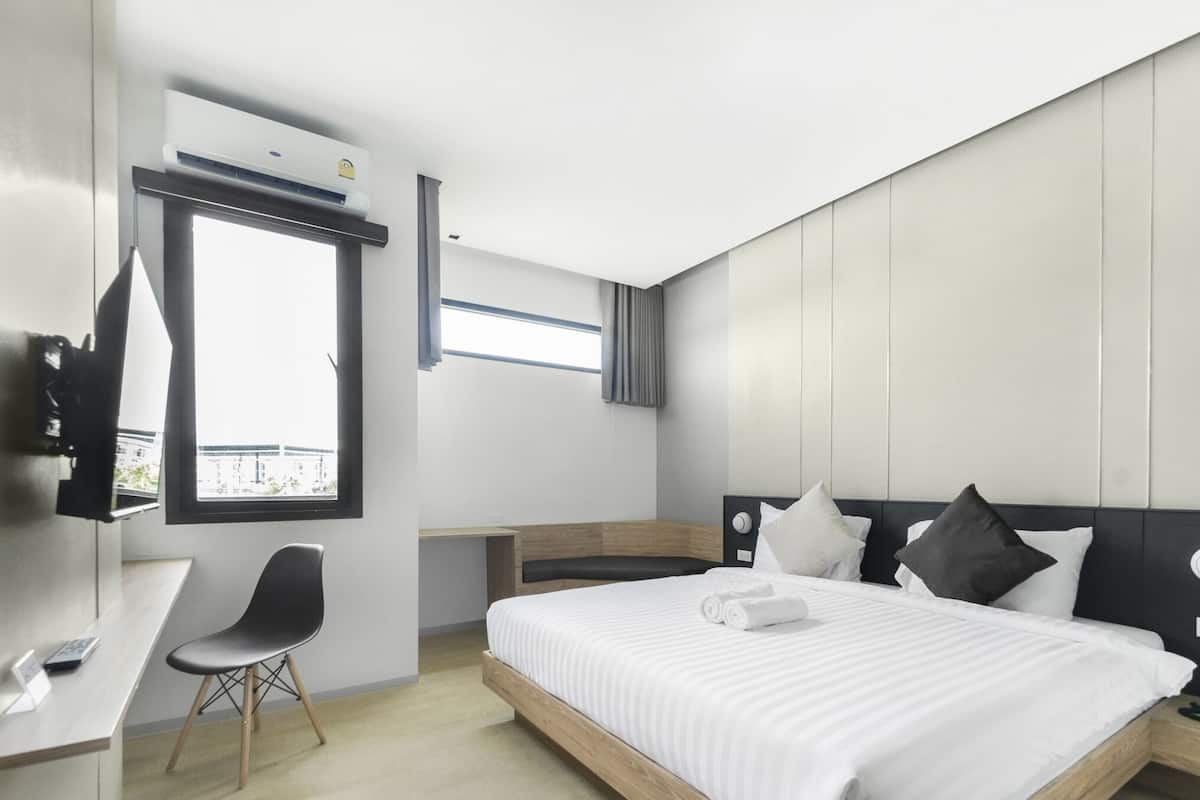 A modern hotel room with a bed, a desk, a chair, a window, and an air conditioning unit.