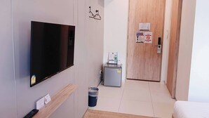 A hotel room with a TV, a desk with a remote, a trash bin, a small fridge, and a wooden door. - B48 Hotel (Bangkok)